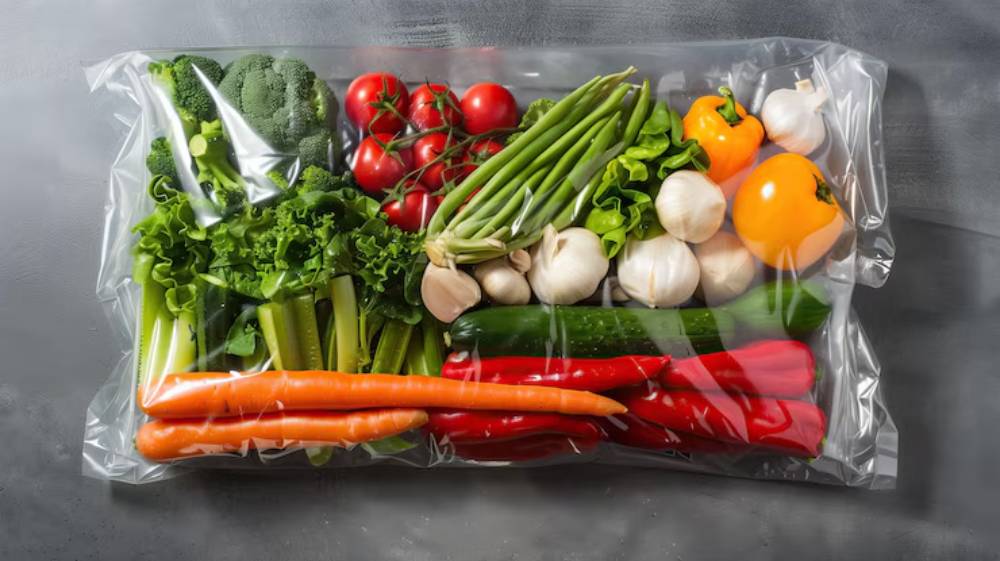 A vacuum-sealed bag filled with fresh vegetables, including broccoli, tomatoes, lettuce, carrots, garlic, and bell peppers.