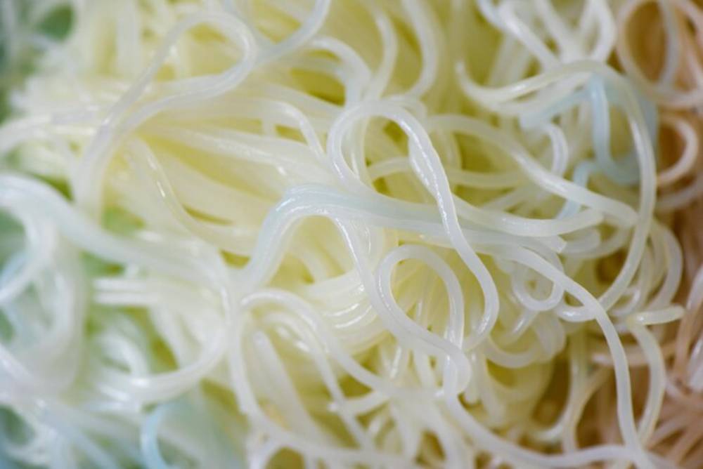 Close-up of translucent, thin gel noodles entwined together, varying from pale white to slightly greenish hues.