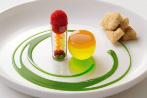 A gourmet dessert featuring a tubular glass filled with colorful fruit, a yellow gelatin sphere, and biscuit pieces on a white plate.