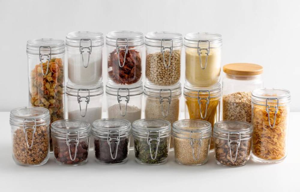 A neatly organized display of various clear jars filled with grains, pasta, herbs, and dried fruits, showcasing a well-stocked pantry.