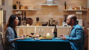 A dining setup featuring two people at a table with a blue tablecloth, candles, wine, and an array of delicious food.
