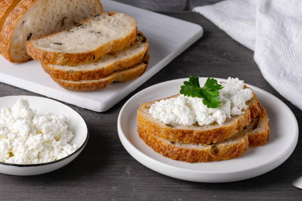 Sliced whole grain bread topped with cottage cheese and garnished with a sprig of parsley, next to a bowl of cottage cheese.