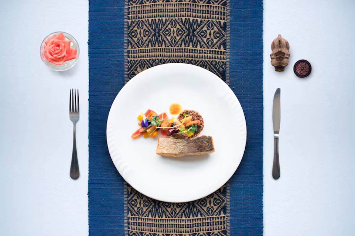 A beautifully plated dish featuring pan-seared fish, colorful garnish, and a side of salad, set on a textured blue tablecloth.