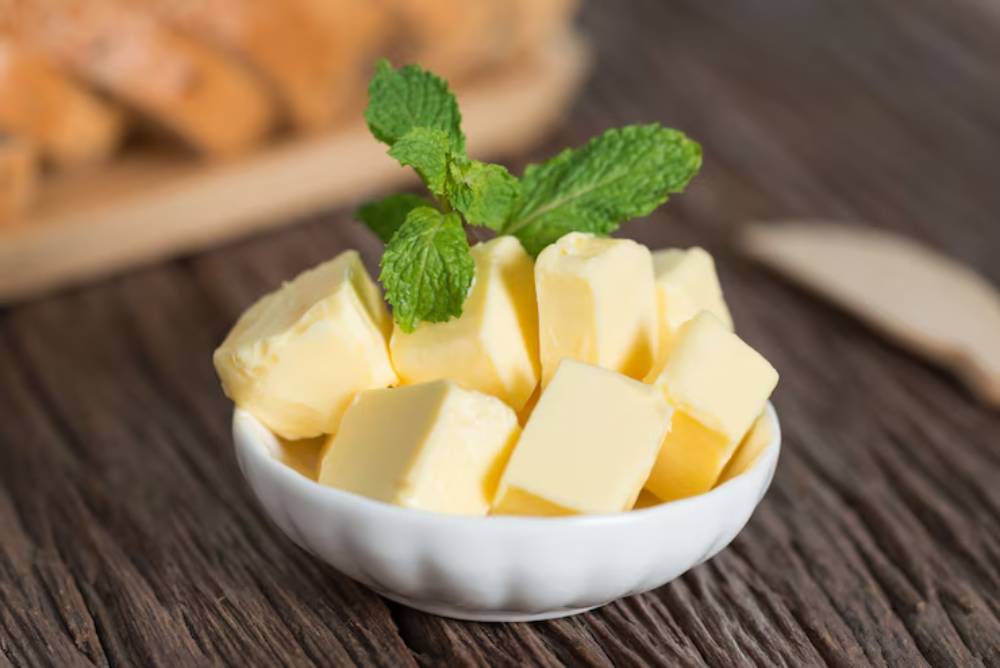 A small white bowl filled with cubed butter, topped with fresh mint leaves, on a rustic wooden surface.