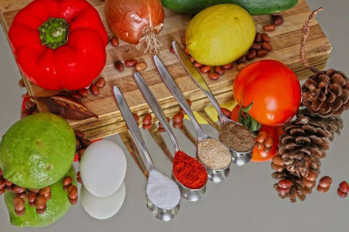 A vibrant assortment of vegetables, spices in measuring spoons, and pinecones arranged on a wooden board.