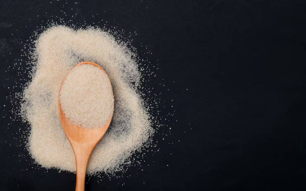 A wooden spoon rests on a mound of agar-agar powder, scattered on a dark surface.