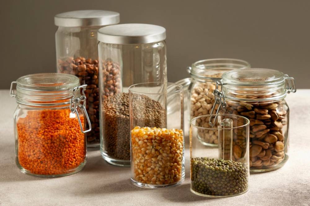 A collection of glass jars filled with various colorful lentils and seeds arranged on a neutral surface, showcasing their textures.